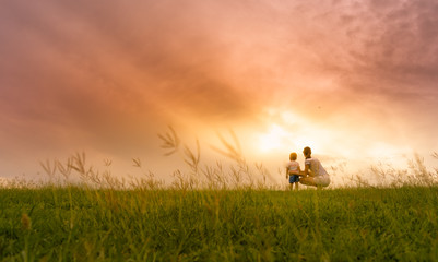 Mother and son spending time together outdoors watching the beautiful sunset in a grass field. 