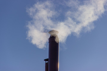 Smoke from the chimney, heating the house in winter..Chimney stacks made of metal with smoke coming up..Smoke in the blue sky..