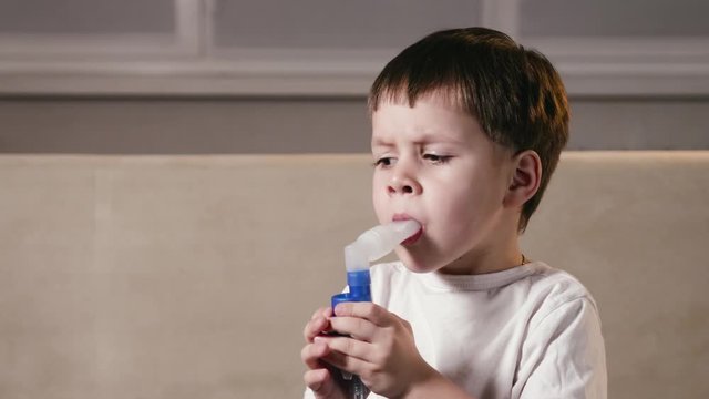 A small, cute boy makes inhalations using a nebulizer at home. A sick child breathes through a spray bottle. Concept of treatment of children's respiratory and lung diseases