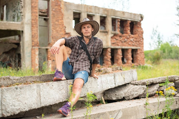 A man in a cowboy hat sits amid a ruined home.