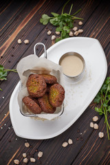 Chickpea  flafel with sauce, on a white plate, on a wooden board. Chickpeas and herbs around the plate