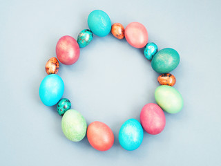 Easter background. Round frame of bright multi-colored Easter eggs on a blue background, top view, copy space. 