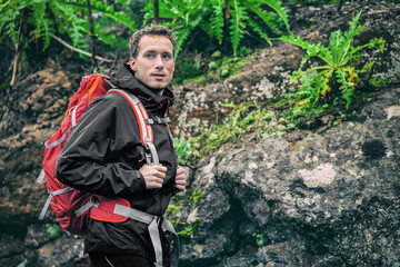 Hiker man hiking in rainforest spring autumn. Male hiker looking away walking in outdoors forest nature trail path. Caucasian male model on adventure trek wearing rain jacket and camping backpack.