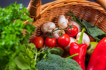 Vegetarian vegetables: mushrooms, peppers, broccoli, tomatoes, herbs in a wicker basket on a black background in the studio