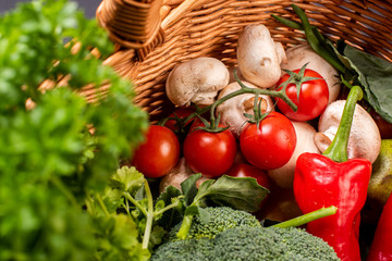 Vegetarian vegetables: mushrooms, peppers, broccoli, tomatoes, herbs in a wicker basket on a black background in the studio
