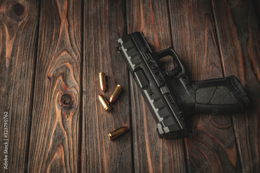 Wall mural Modern black gun and ammunition  on a wooden background. Pistol. Weapons for sport and self-defense lie on the table.