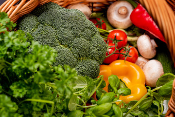 Vegetarian vegetables: mushrooms, peppers, broccoli, tomatoes, herbs in a wicker basket on a black background in the studio