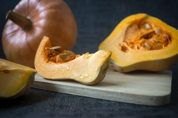 Beautiful ripe pumpkins against a dark background, sliced and whole.
