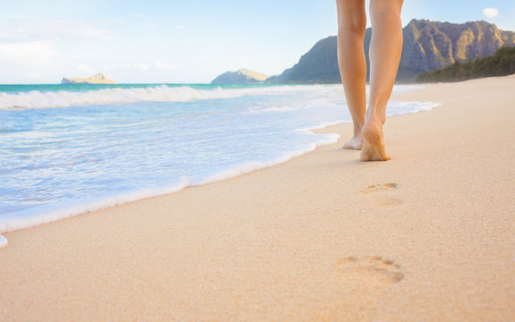 Female walking barefoot on white sand beach leaving footprints in the sand. Location Hawaii. 