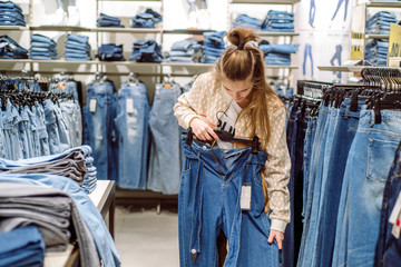 Woman choosing jeans in clothing store. teen girl buys jeans in the mall.