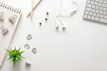 Top view of a white office desk. Office supplies. Copy space. White technology. Keyboard, headphones, notebook and succulent. White on white.