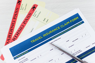 Travel insurance policy claim form with a boarding pass and passport on white wooden table.