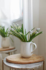Green flowers in a white ceramic vase on a wooden board white mirror in cozy interior 