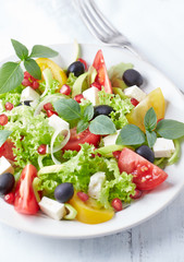 Salad with black Olives, red and yellow Tomatoes, Feta Cheese and Pommegranate Seeds on bright wooden Background. Healthy Snack Idea. 