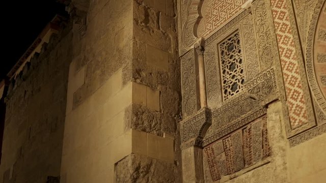 Pan shot right to left of detail facade of Mosque-Cathedral, Cordoba. Facade, side, walls of Mosque-cathedral at night time, Spain