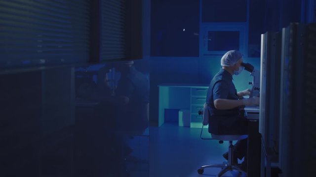 In a Modern Laboratory Scientist Conduct Experiments. Chief Research Scientist Adjusts Specimen in a Petri Dish and Looks on it Into Microscope.