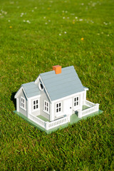 Miniature house with white picket fence standing in the center of lush green grass lawn