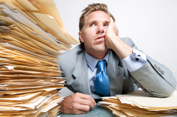 Bored office worker looking overwhelmed at the huge pile of paperwork on his desk