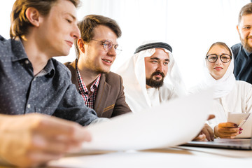 Presentation on a laptop with foreign representatives. A young guy shows information on a laptop to foreign representatives of Arab culture.