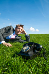 Bored office worker waiting for the phone to ring outdoors in a green meadow 