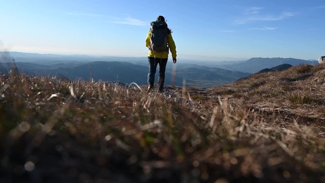 Low angle locked down shot of a female hiker walking past on a mountain path in sunshine