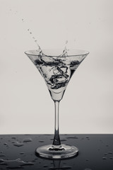 a glass of martini and splashes of liquid from an ice cube