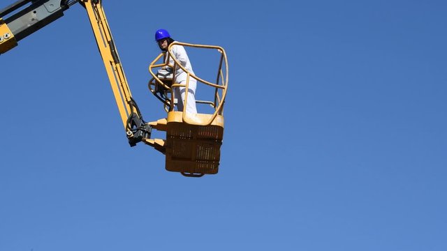 Focused woman operates the control panel of a telescopic boom lift to lower its platform in slow motion.