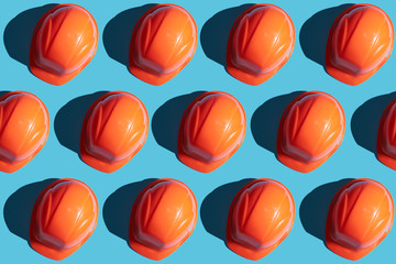 orange safety helmet rows on a blue background with hard shadows. looking from above.industrial pattern backdrop.