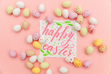 Happy Easter concept. Inscription HAPPY EASTER letters candy chocolate eggs and jellybean sweets isolated on trendy pastel pink background. Simple minimalism flat lay top view copy space.