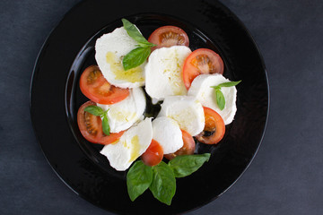 Caprese salad on a large black plate.