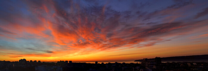 Panorama of dawn fire in the sky over a small seaside city. Golden red clouds just before the sunrise. Scenic landscape at sunrise.