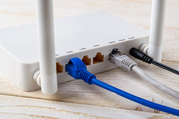 Close-up of network cables connected to a white Wi-Fi wireless router on a white wooden table. Wlan...