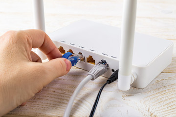 Woman hand plugging a blue network cable into socket of a white Wi-Fi wireless router on a white...