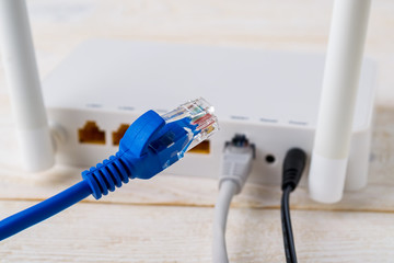 Close-up of blue network cable on a background of a white Wi-Fi wireless router on a white wooden table. Wlan router with internet cables plugged in on a table in a home or office. - obrazy, fototapety, plakaty