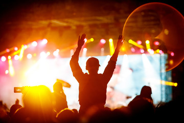 The crowd with their hands up enjoys music concert. Fan silhouette on stage background.