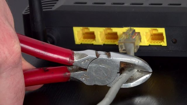 A pair of wire cutter diagonal pliers are shown cutting an ethernet internet cord connected to a modem.
