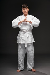 Fototapeta na wymiar a teenager dressed in martial arts clothing poses on a dark gray background, greeting position, sports concept