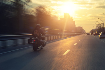 Silhouette of biker riding black chopper motorcycle on city street highway road and sunset bright...