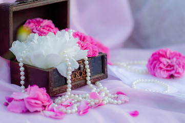 Floral arrangement of pink roses flowers and peonies in a wooden box with pearl beads on a pink...