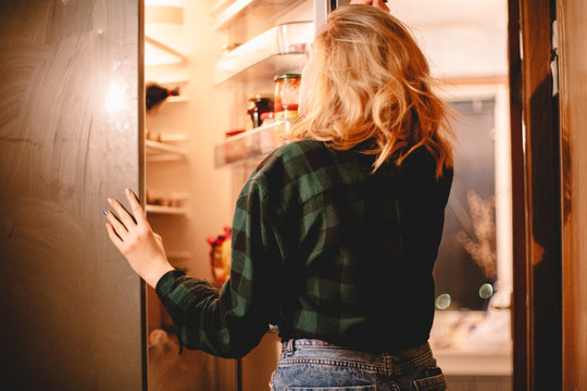 Young hungry woman looking in open fridge at home