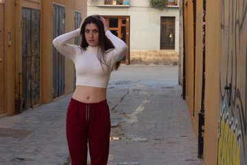 Portrait of attractive caucasian young woman keeps hand on head, grimaced, has problems, being in bad mood, has terrible headache, in the city, white top and red pants, dark air. Place for your text i