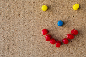 Smiley face made with pins on a cork board