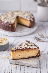 Piece Slice of Сheesecake with Chocolate, Caramel, Peanut Paste, Nougat Layered Cake on white table background