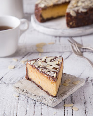 Piece Slice of Сheesecake with Chocolate, Caramel, Peanut Paste, Nougat Layered Cake on white table background