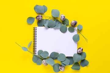 Happy Easter greeting card with blank white notepad, eucalyptus leaves and quail eggs on bright yellow background.
