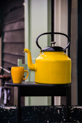 A vintage yellow kettle and a yellow cup on a little wooden shelf