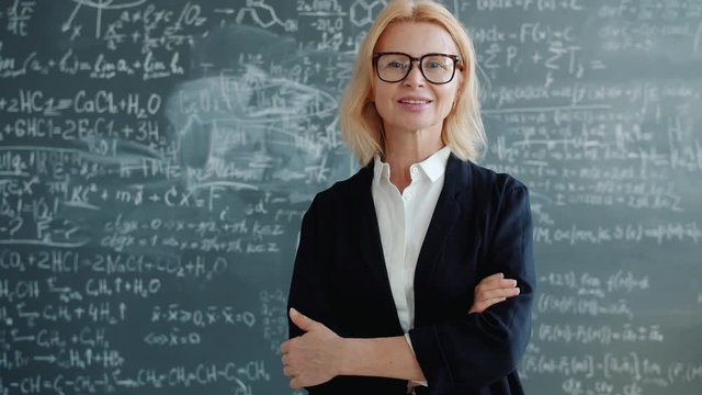 Portrait of friendly lady teacher standing in classroom with arms crossed alone smiling and looking at camera. People, lifestyle and occupation concept.