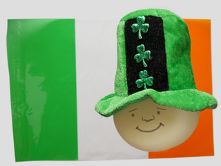 Green hat with shamrock on a round shape sponge head, funny smiley face. Irish flag in the...
