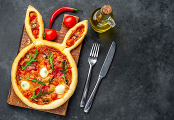 Easter rabbit pizza with eggs  on a cutting board with a fork and knife on a stone background with copy space for your text