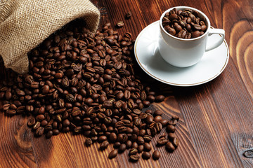 Roasted coffee beans on a wooden background with next to a white cup. Fresh drink.